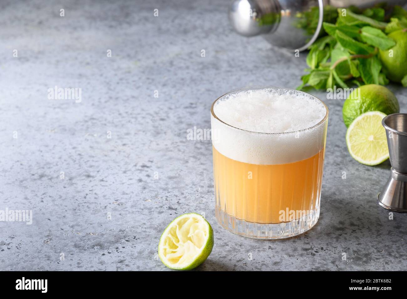 Pisco sour cocktail whiskey with lime, egg white, sugar syrup in glass on grey stone table