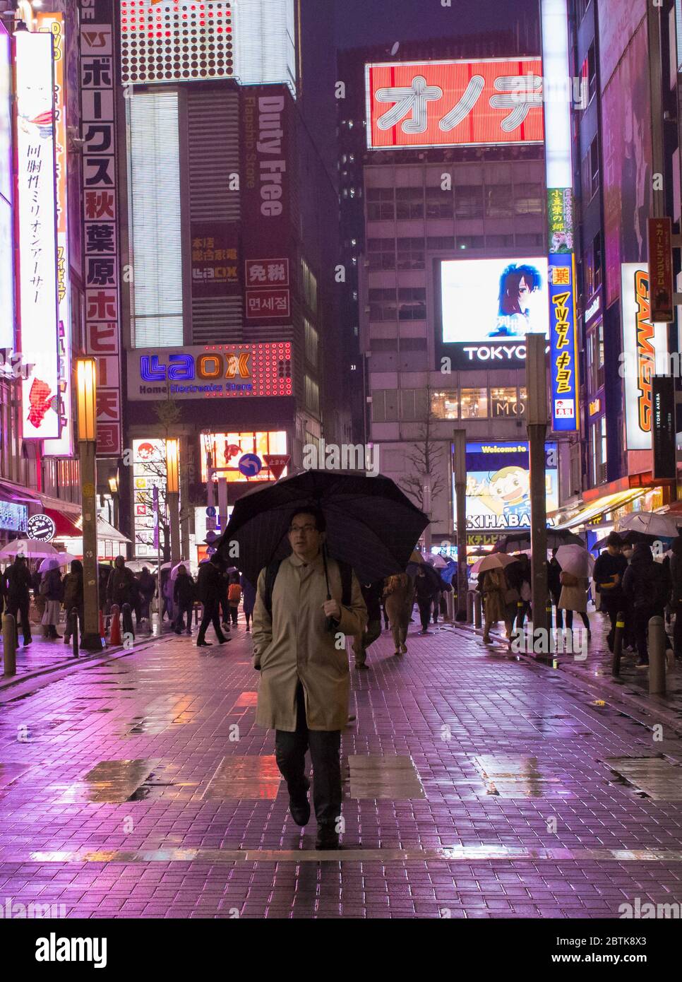 The neon shop lights of Akihabara in the rain with a man holding an umbrella. Tokyo, Japan Stock Photo