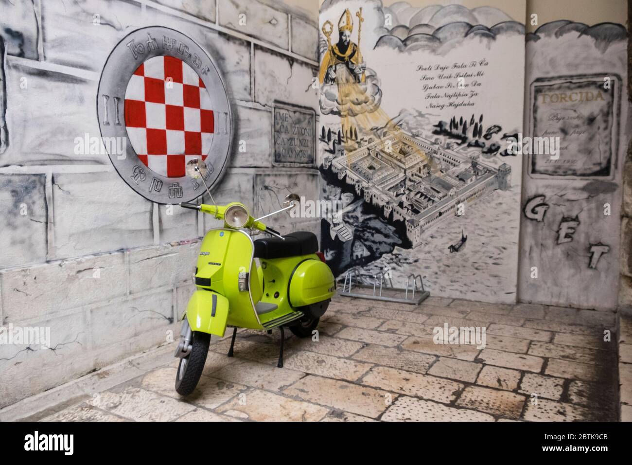Green vespa parked beside stone wall that features a painted logo of Croatian football club HNK Hajduk Split, in Old Town Stock Photo