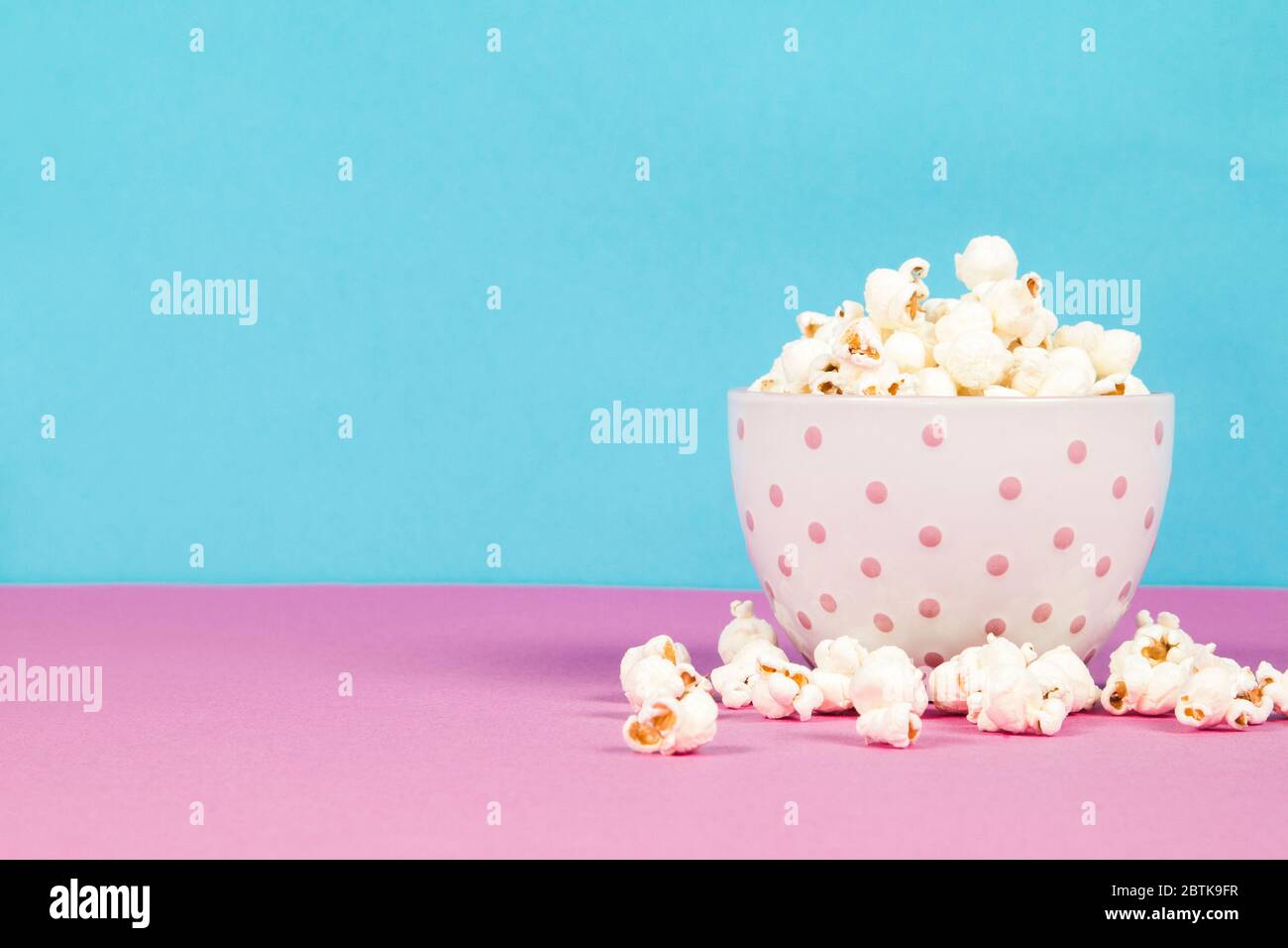 Fresh popcorn in a white pink bowl on pink and blue background Stock Photo