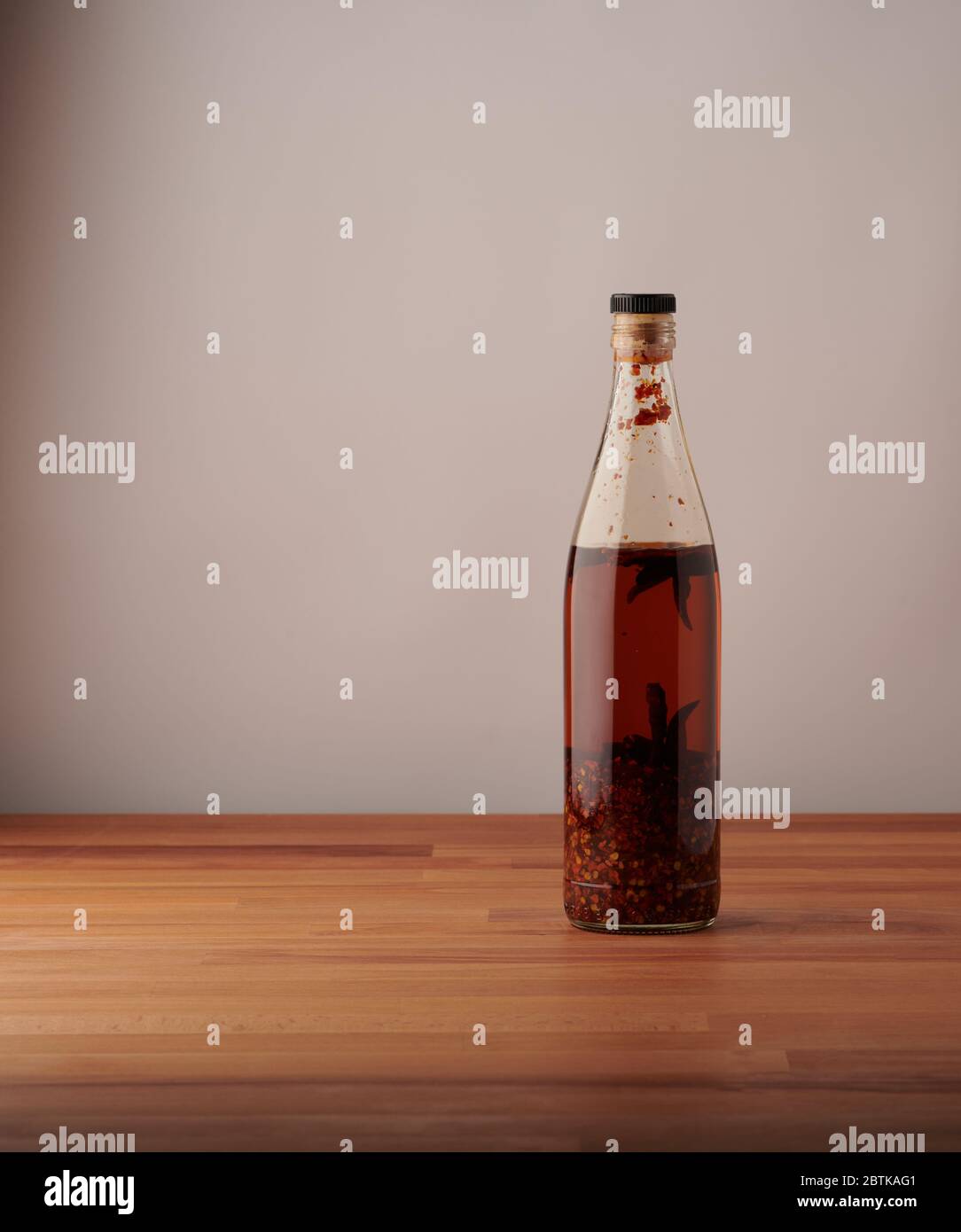 Transparent bottle of homemade chilli oil with pieces of dry chilli, on a wooden table Stock Photo