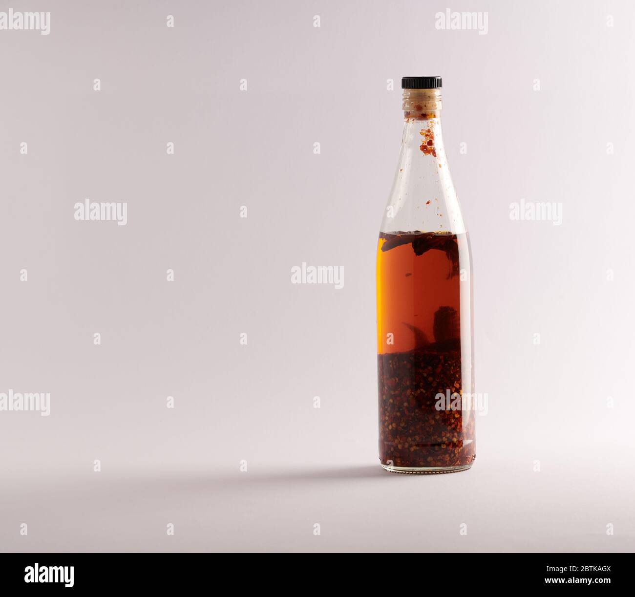 Transparent bottle of homemade chilli oil with pieces of dry chilli, on a white background Stock Photo