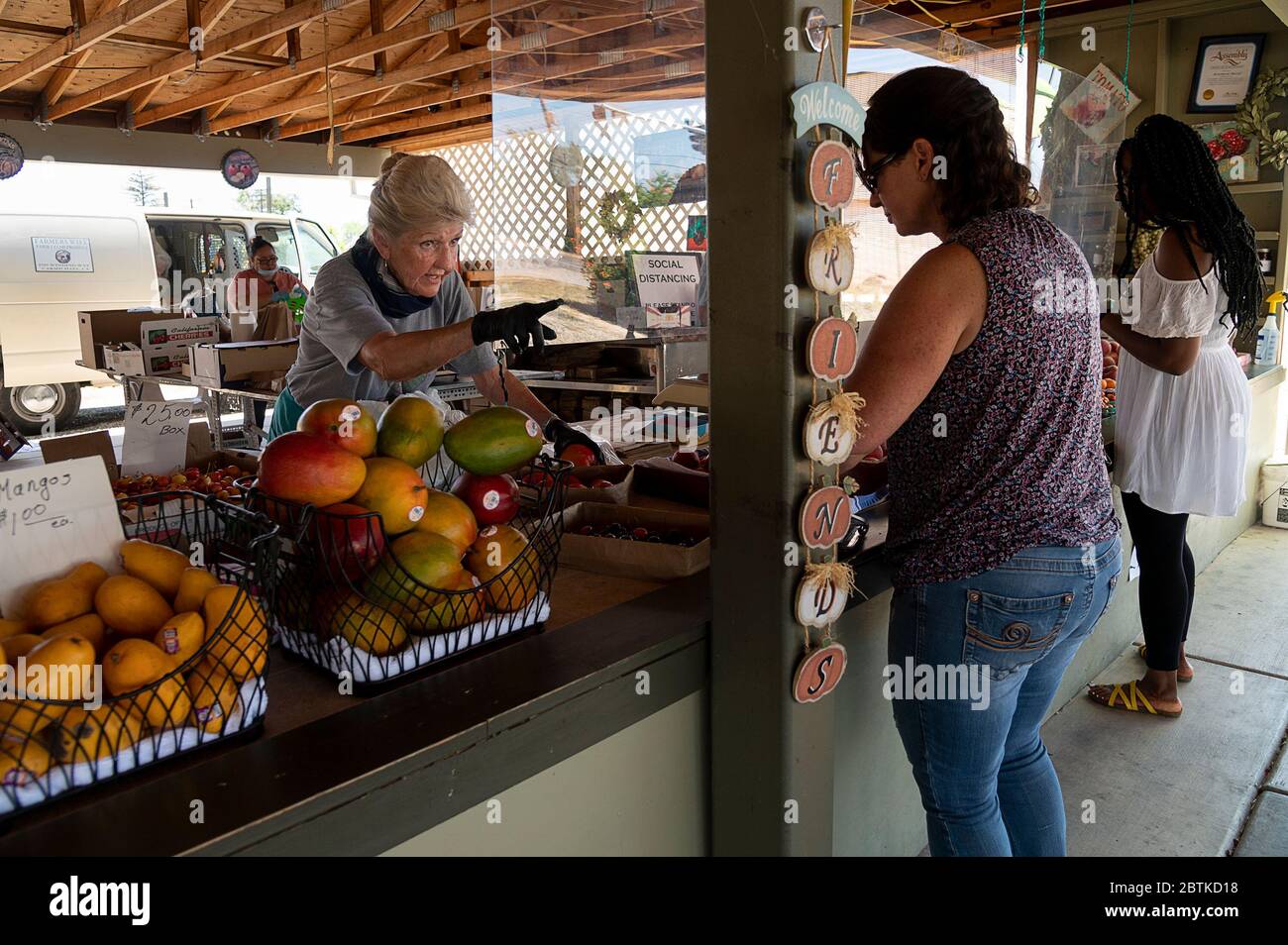 Carmichael, CA, USA. 26th May, 2020. Rosemarie Martell wearing gloves talks with her customer Anita Myers of Grass Valley behind a plastic shield at the Farmer's Wife on Tuesday, May 26, 2020 in Carmichael during the coronavirus pandemic.Martell runs the Farmers Wife produce stand 7 days a week and has been open throughout the pandemic. Many of her customers feel safe shopping at the open air market. Credit: Paul Kitagaki Jr./ZUMA Wire/Alamy Live News Stock Photo