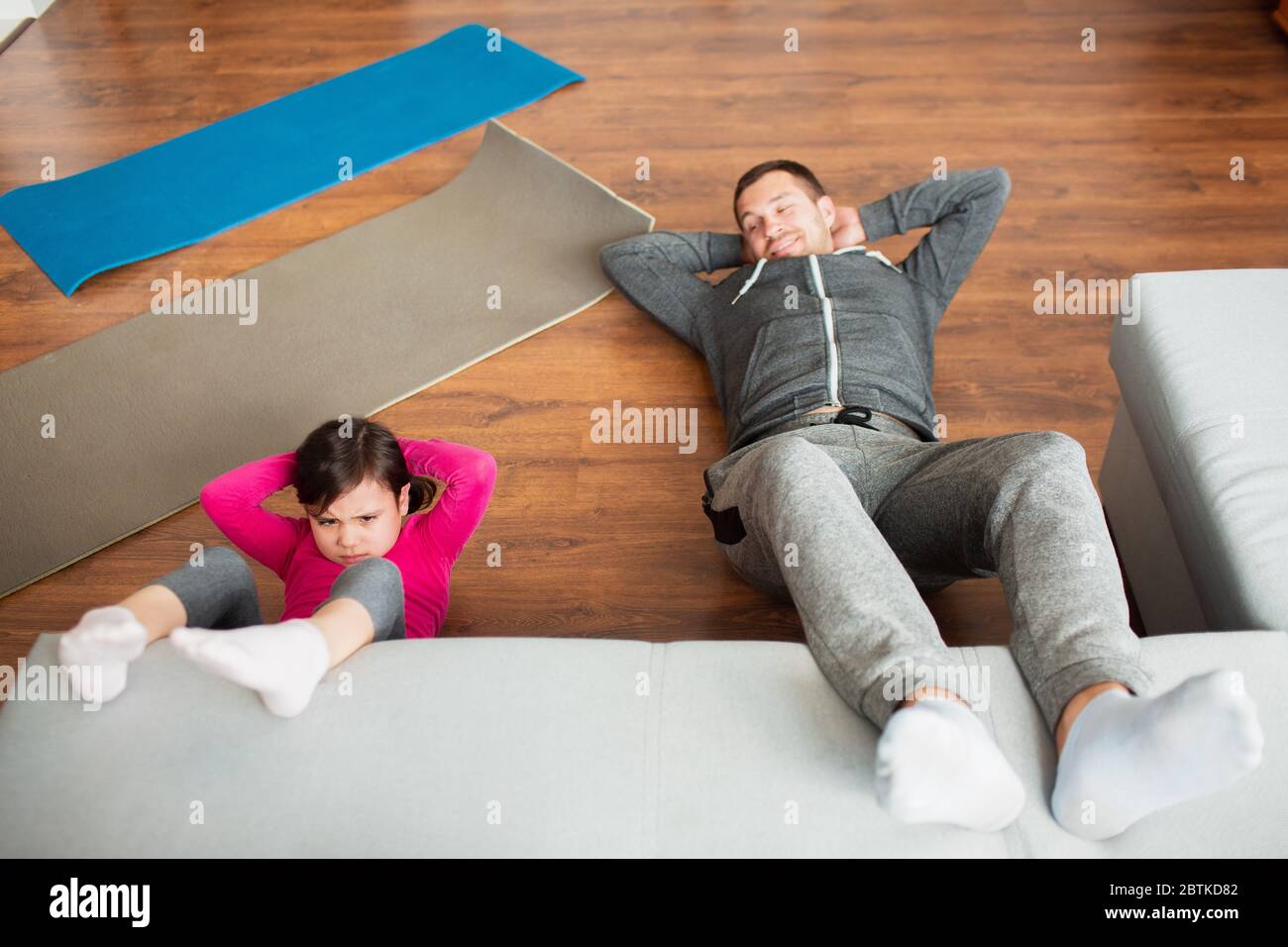father and daughter are doing abs training at home. Workout in the apartment. Sports training in the living room. Stock Photo