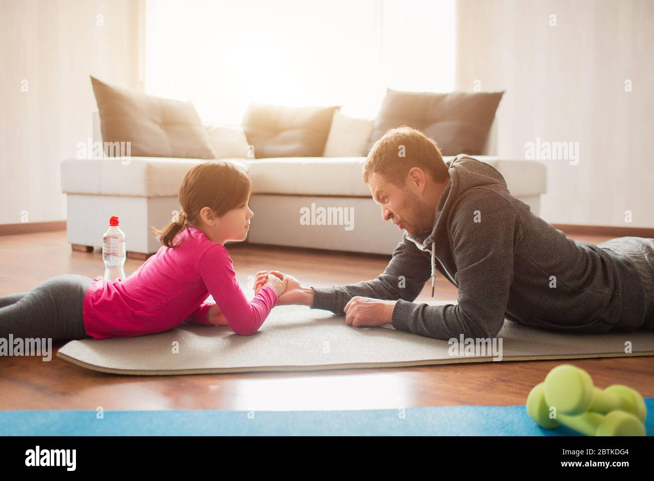 father and daughter are training at home. Workout in the apartment. Sports at home. Compete in arm wrestling and lie on a yoga mat. Stock Photo