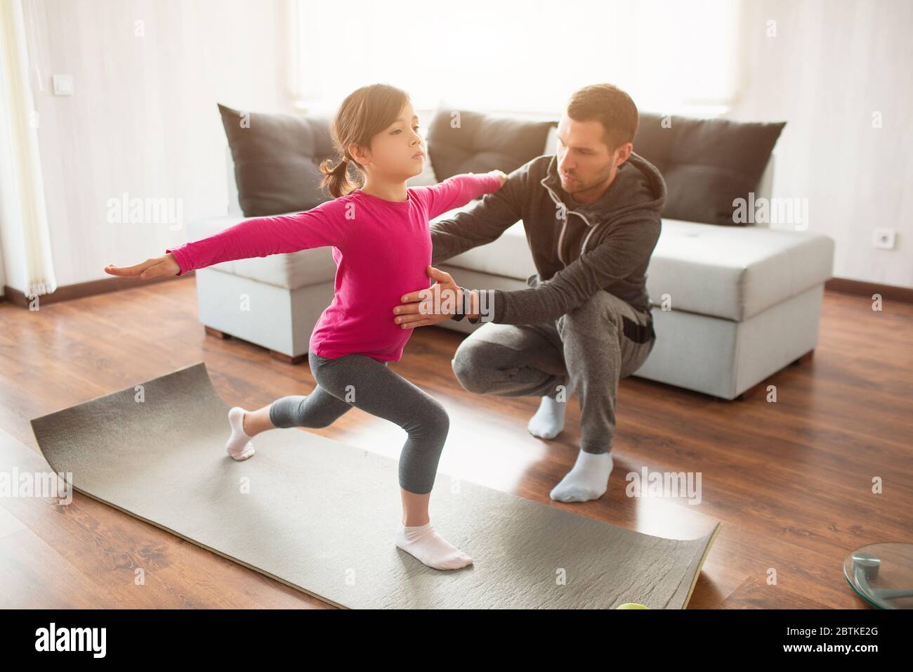 Little girl and her young father are doing lunge forward workout at home. Cute kid is training indoor. Little dark-haired female model in sportswear h Stock Photo