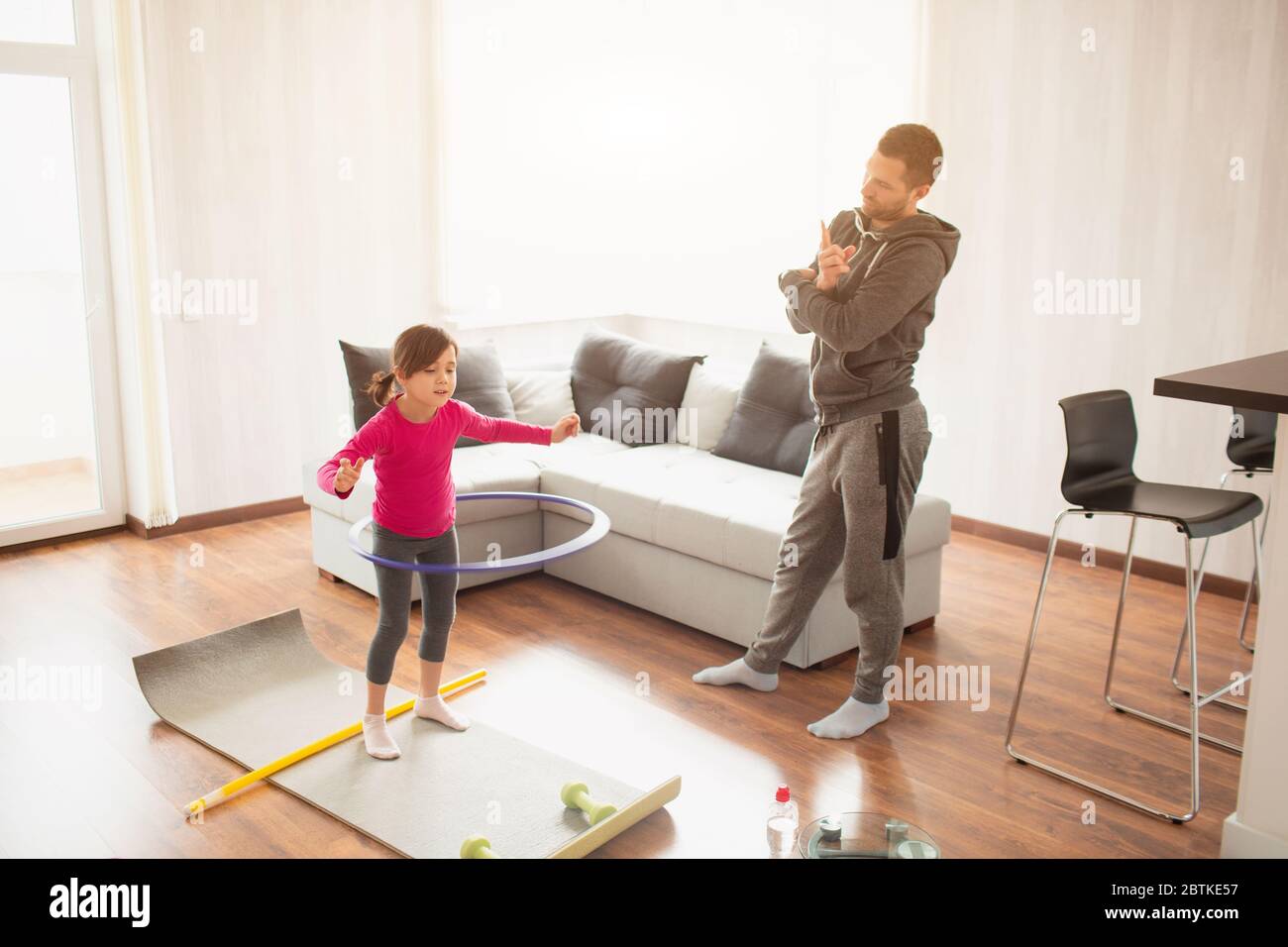 father and daughter are training at home. Workout in the apartment. Sports at home. she tweaks a hula hoop and dad uses a sports watch to measure time Stock Photo