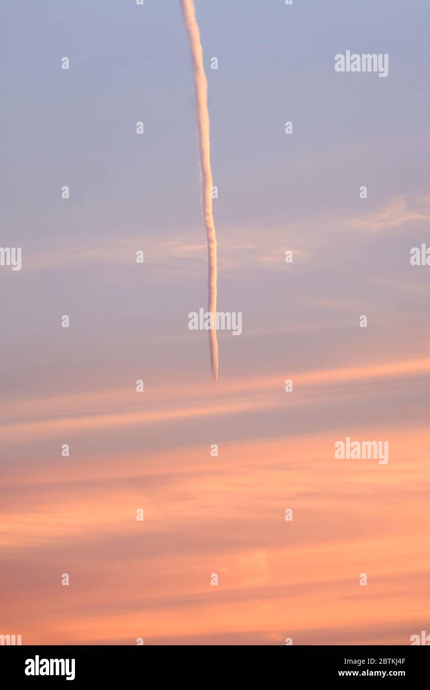 An aeroplane vapour trail reflects light during sunset. Stock Photo