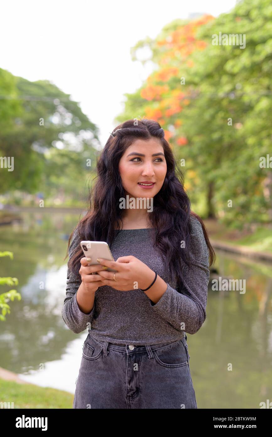 Happy young beautiful Indian woman thinking while using phone at the ...