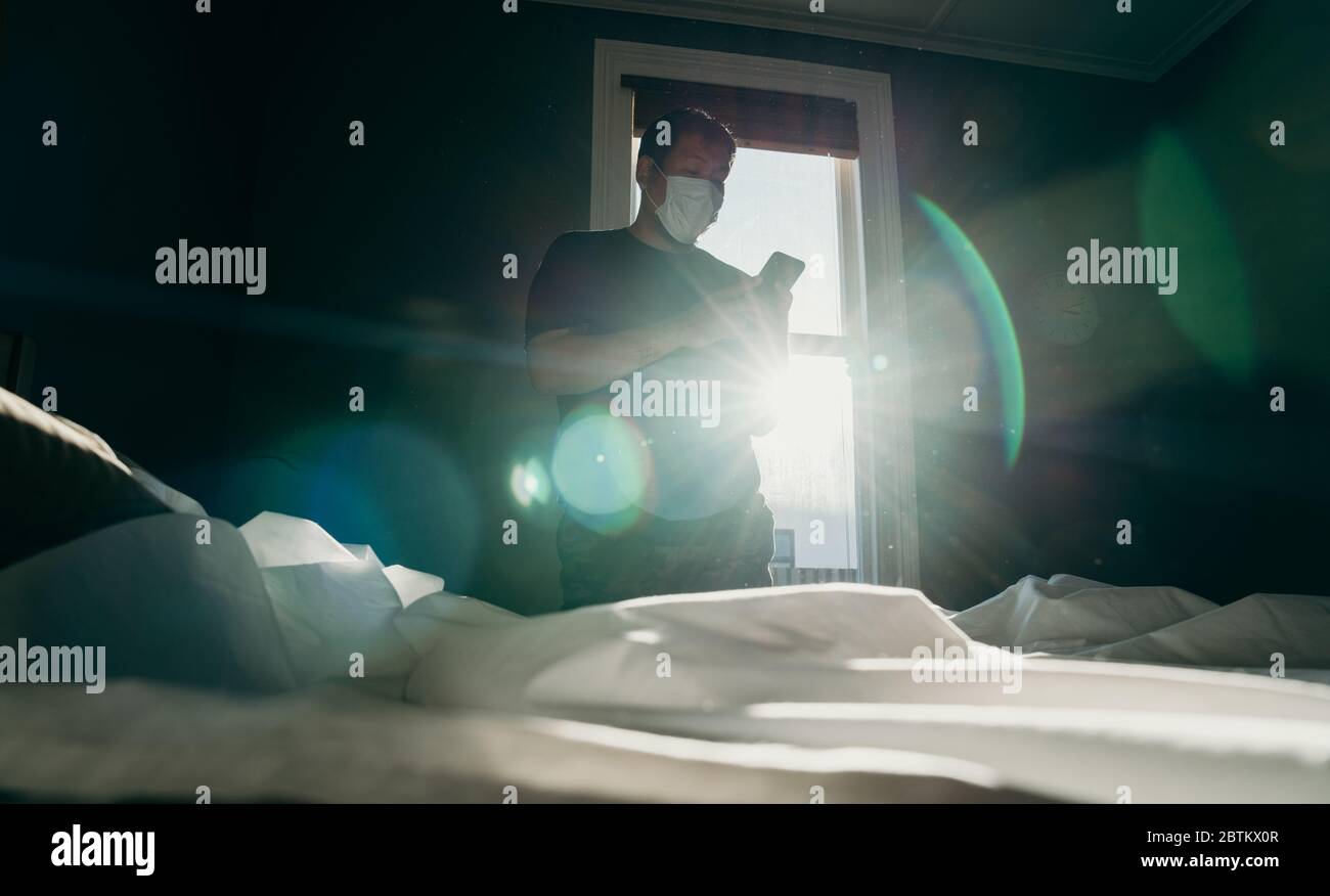 Asian man cleaning bed in morning and using cellphone. House keeping action. Bedroom gainst the sun light. Stock Photo