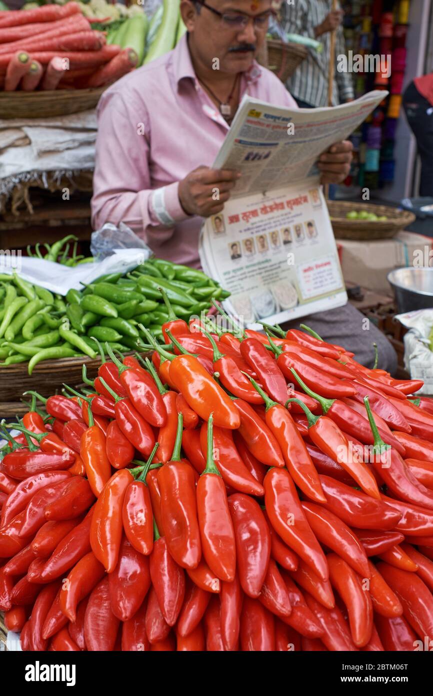 Red and green chilis on a sale at a roadside vegetable stall in Mumbai, India, the vendor engrossed in his newspaper Stock Photo