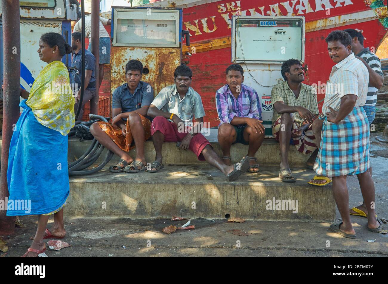 South Indian fisherman at the Old Port in Mangalore, Karnataka, South India, resting at a rusty old petrol pump, a fishing trawler in the background Stock Photo