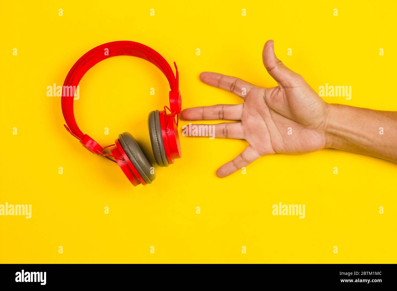 hand holding Red headphones on yellow background. Music concept Stock Photo