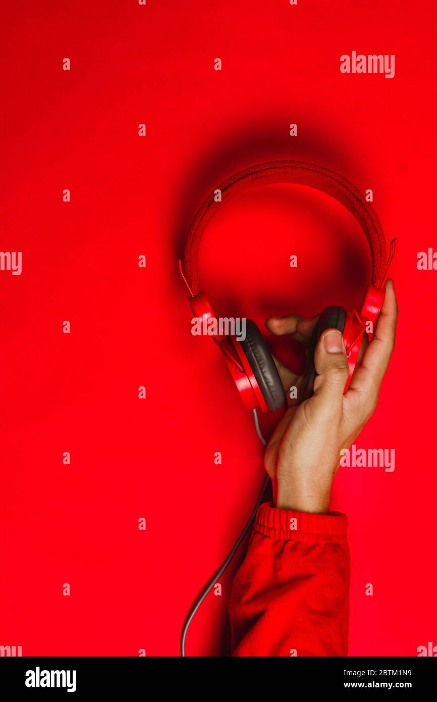 hand holding Red headphones on red background. Music concept Stock Photo