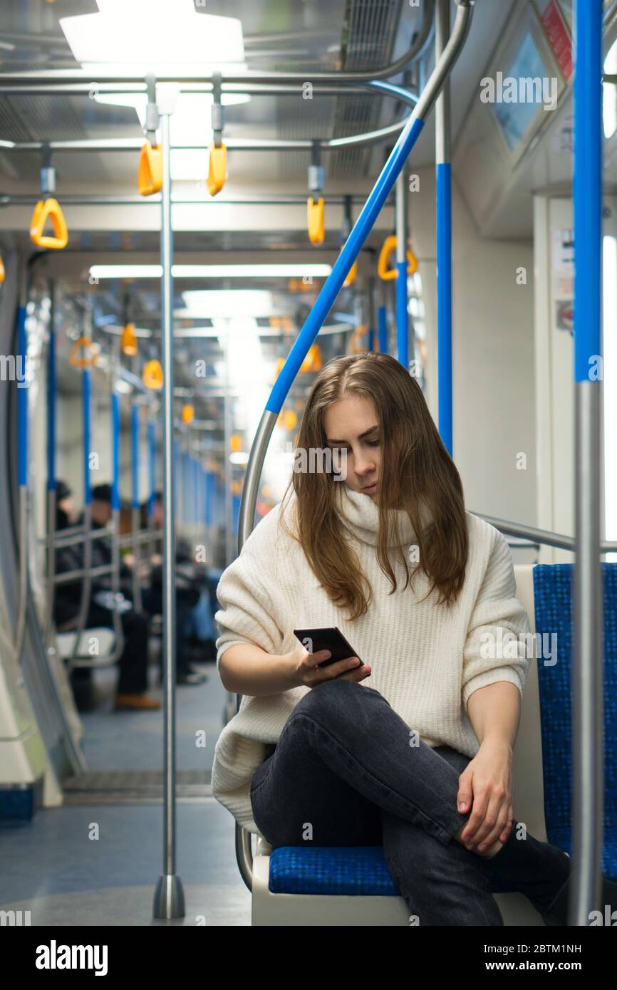 Beautiful woman tourist of appearance in subway car and looks at screen of her smartphone, plotting route. Portrait of female passenger using mobile phone in subway train. Stock Photo