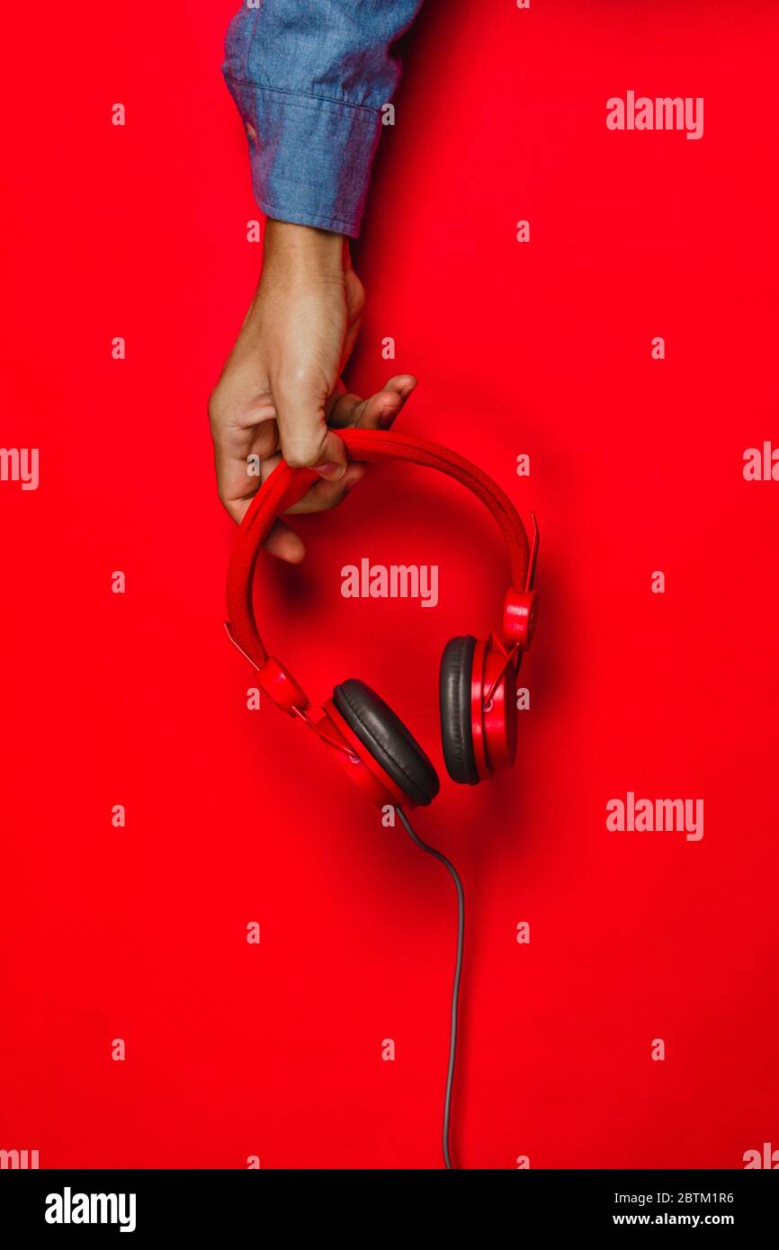 hand holding Red headphones on red background. Music concept Stock Photo