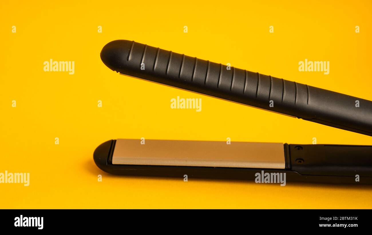Professional hair iron for straightening hair on yellow background with copy space Stock Photo