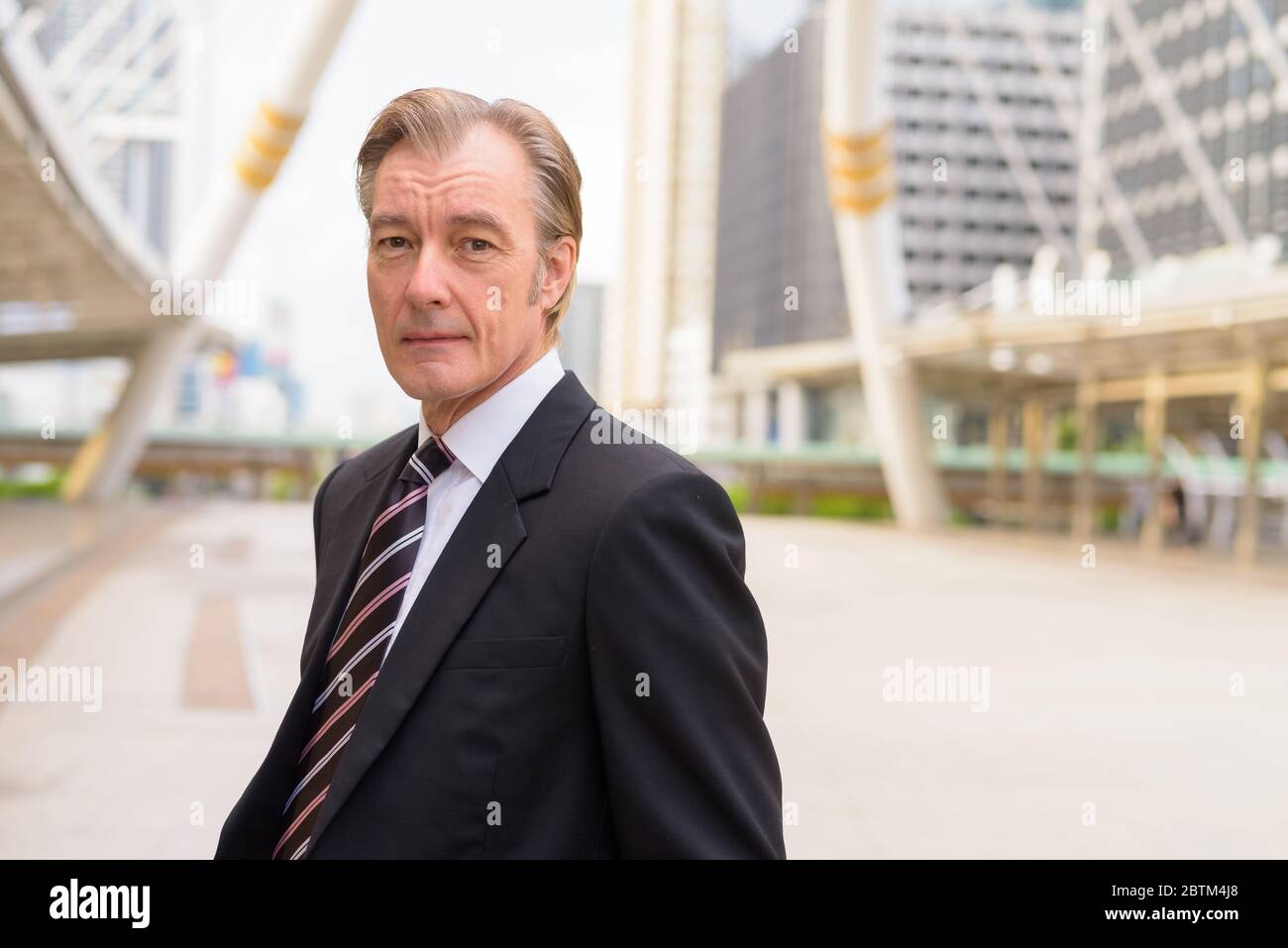 Mature handsome businessman in suit at skywalk bridge in the city Stock ...