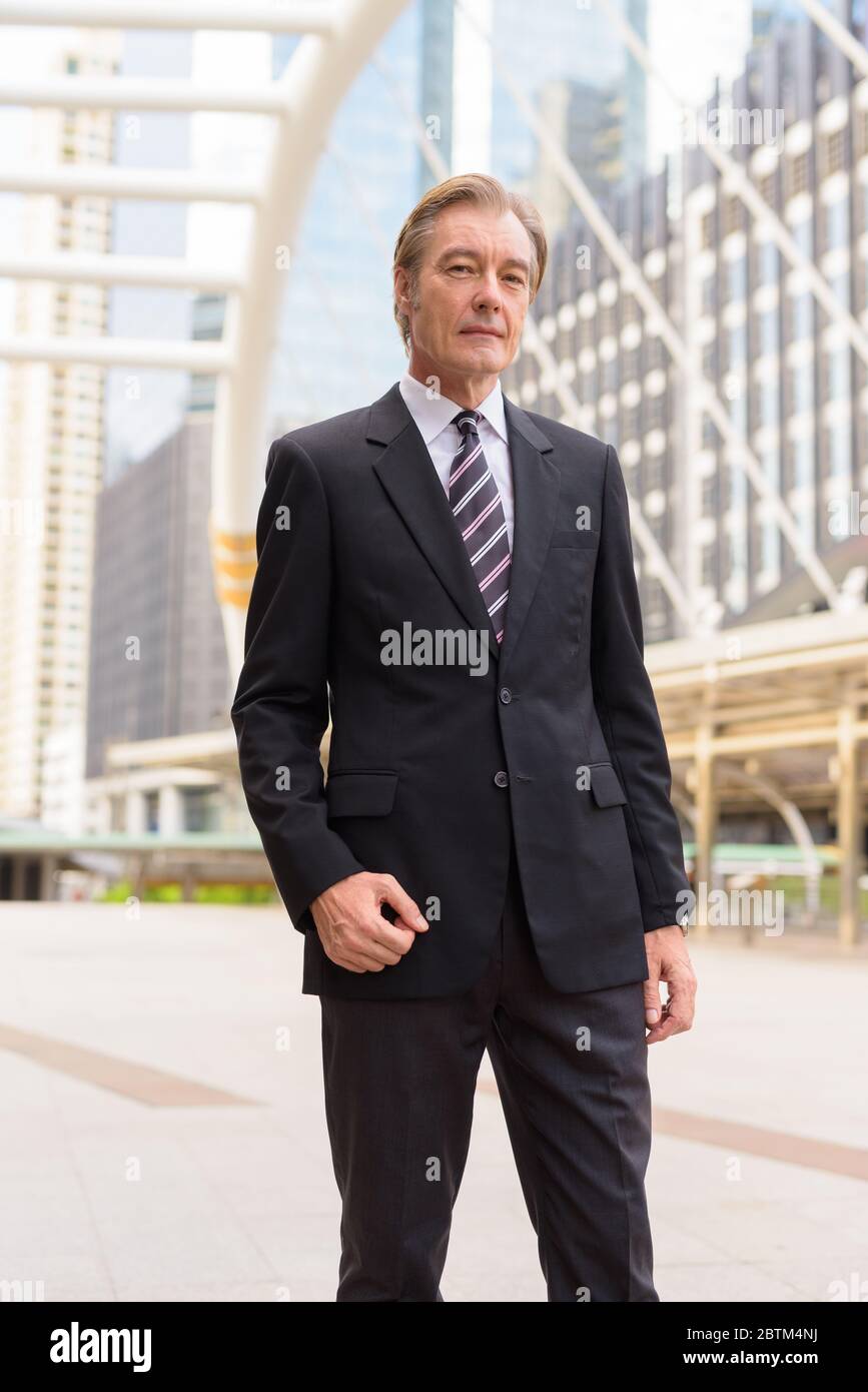 Mature handsome businessman in suit at skywalk bridge in the city Stock ...