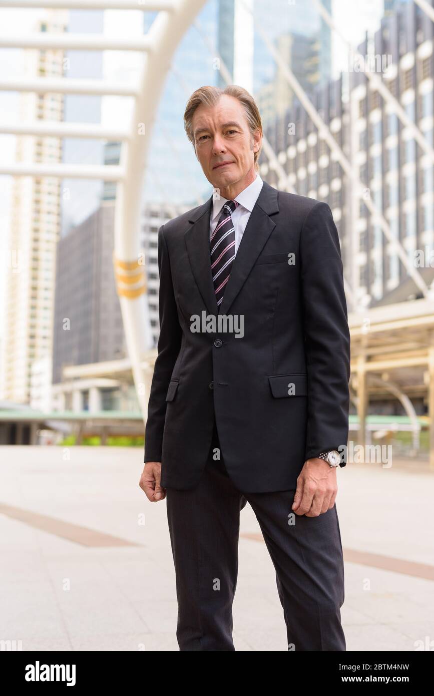 Mature handsome businessman in suit at skywalk bridge in the city Stock ...