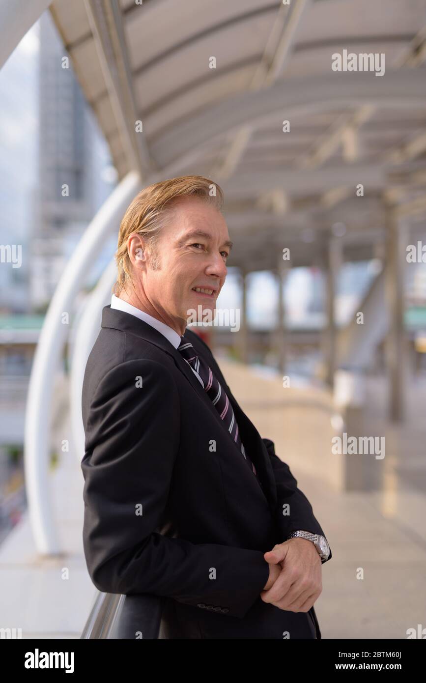 Happy mature handsome businessman in suit leaning at footbridge in the ...