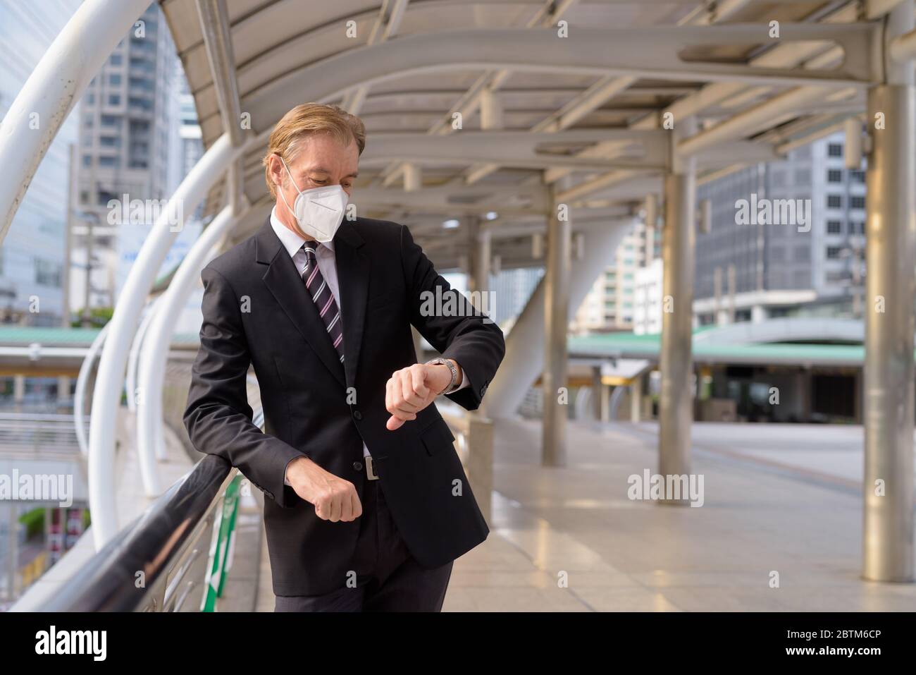 Mature businessman with mask checking the time at the footbridge Stock ...