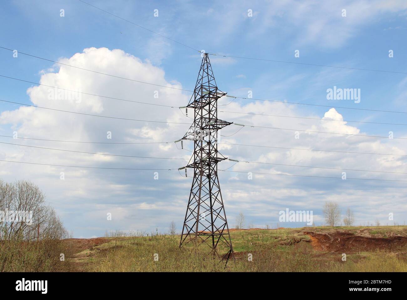 Iron pylon of a high voltage power line stands in a field against a blue sky. Stock Photo
