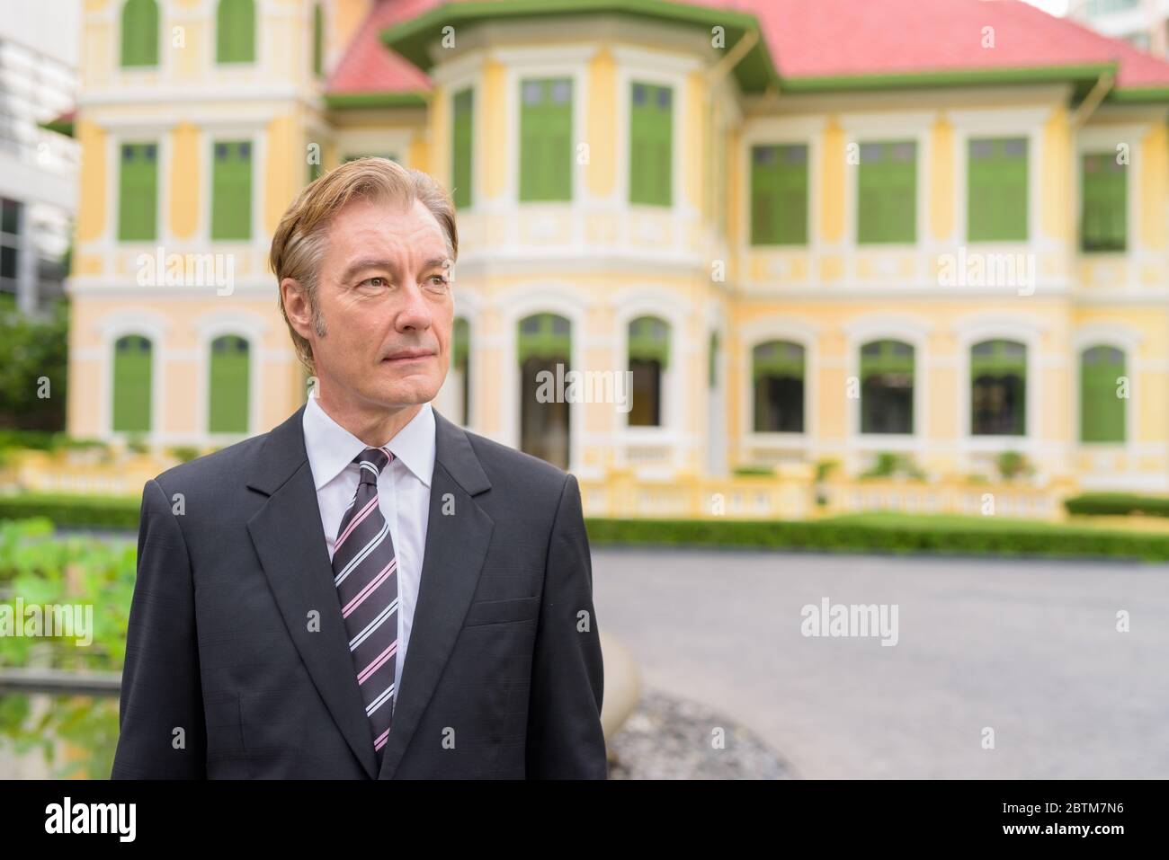 Mature handsome businessman wearing suit and thinking in the city ...
