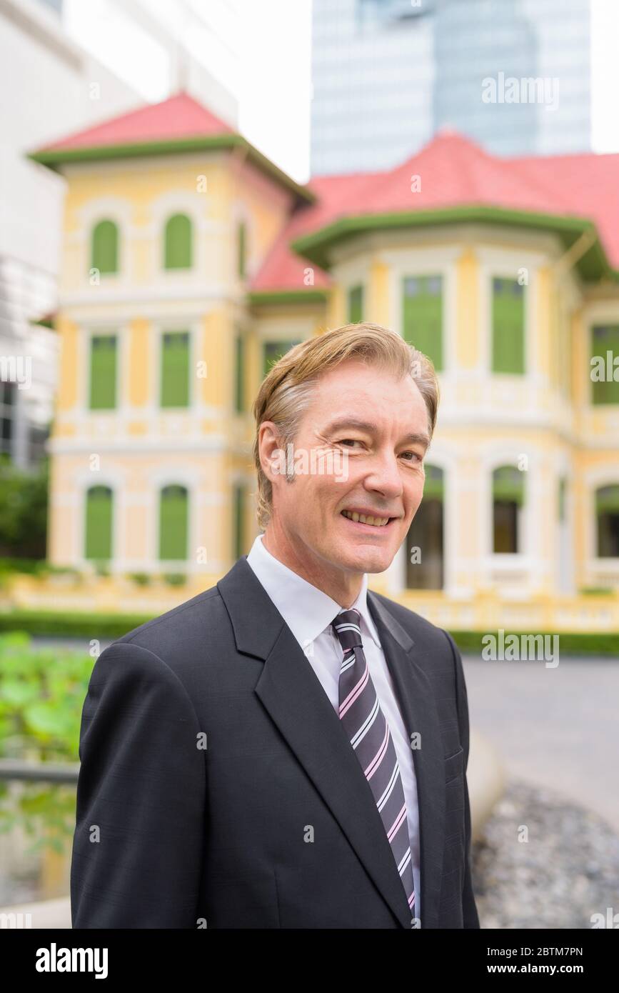 Happy mature handsome businessman in suit smiling in the city outdoors ...