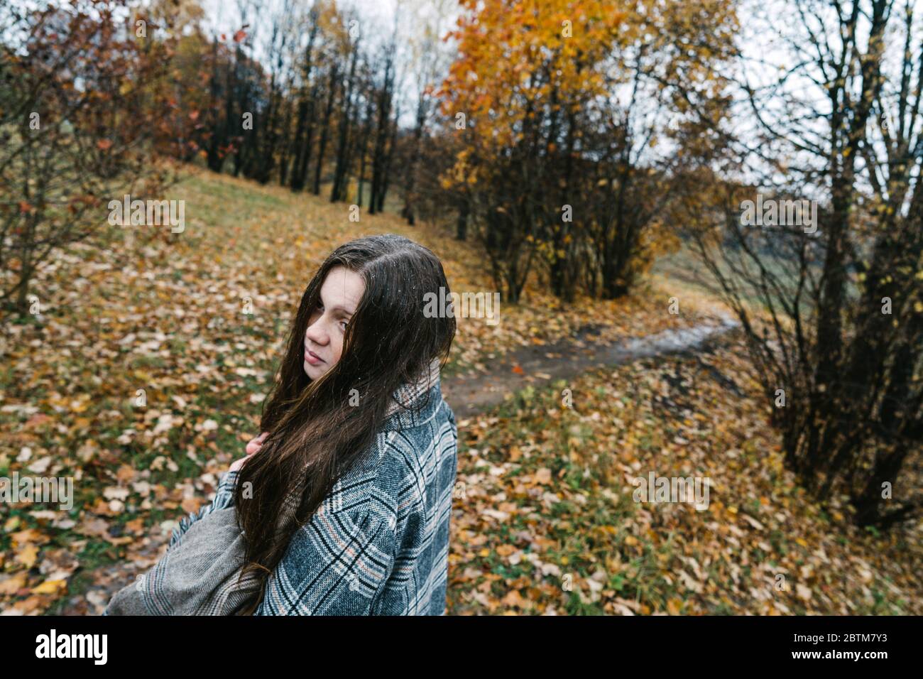 Red-headed freckled girl in autumn yellow park. The first snow, wet rain. Stock Photo