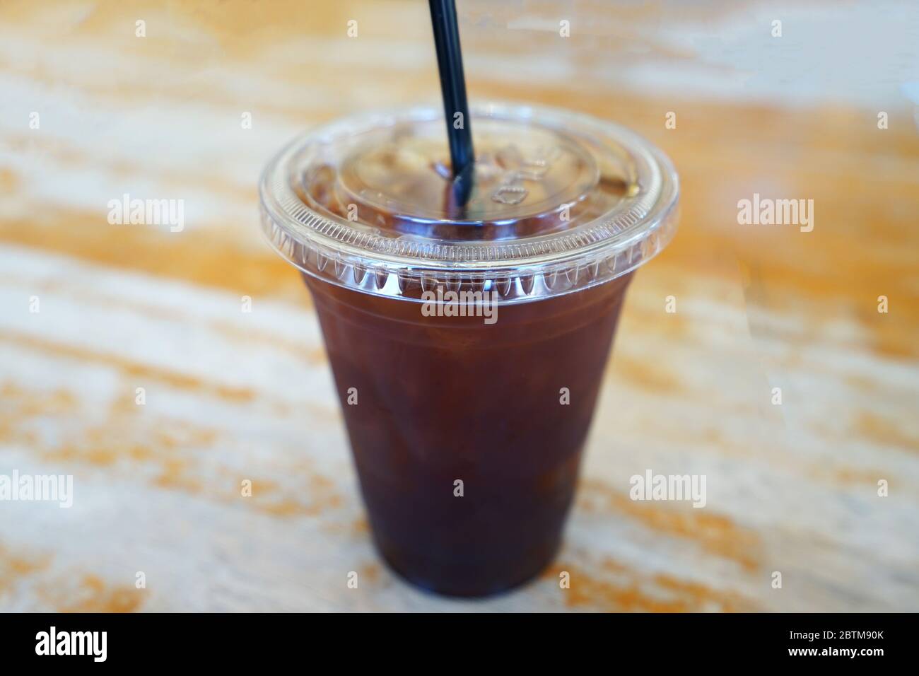https://c8.alamy.com/comp/2BTM90K/close-up-take-away-plastic-cup-of-iced-black-coffee-on-wooden-table-2BTM90K.jpg