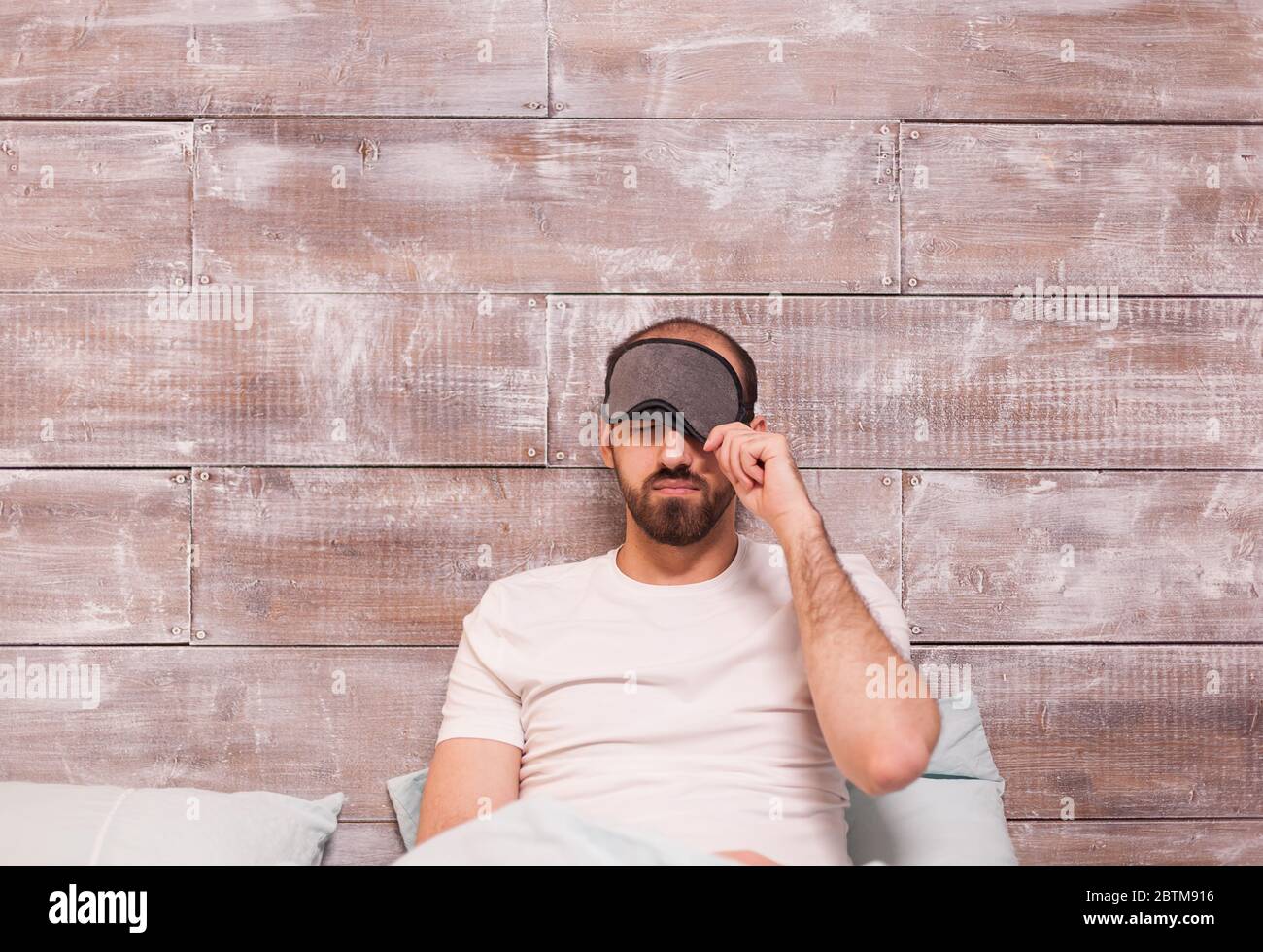 Man pulling his sleep mask before going to sleep in comfortable bed. Stock Photo