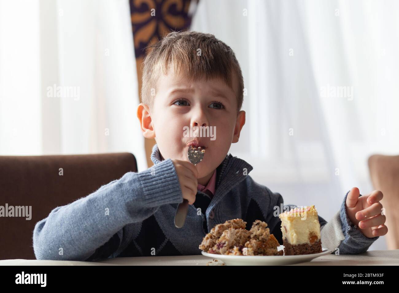 Cute little boy in cafe eat a big piece of cake with a fork. Desserts