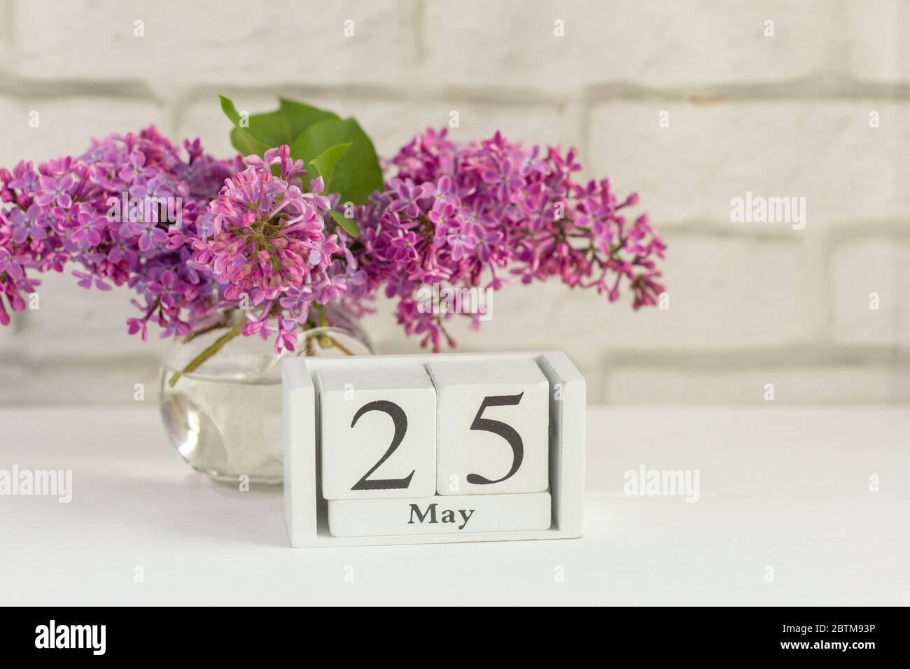 May 25 on a wooden calendar next to a bouquet of lilacs.One day of the spring month.End of the school year.Last call at school. Stock Photo