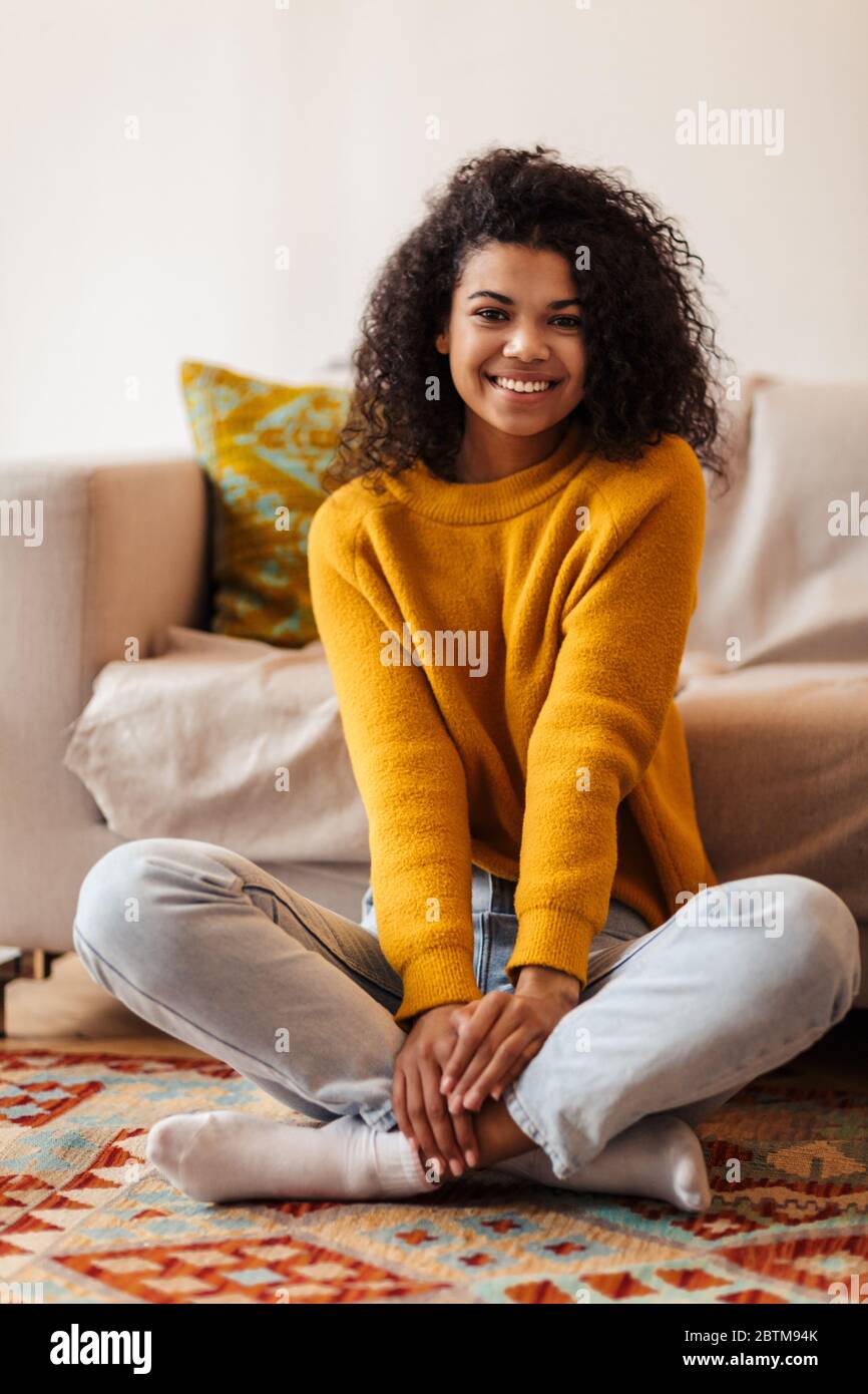 Image of joyful african american woman smiling while sitting on floor ...