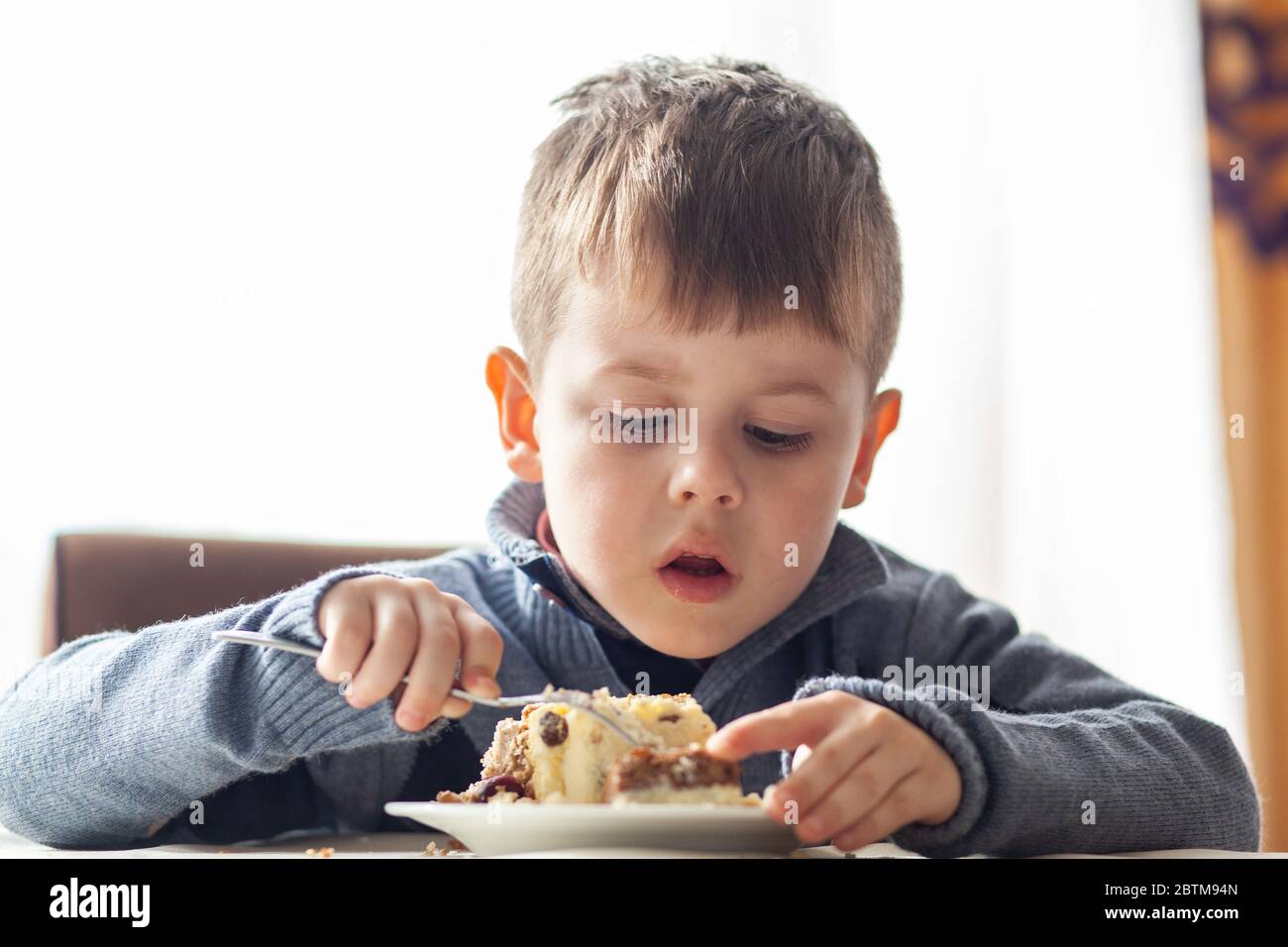 Cute little boy in cafe eat a big piece of cake with a fork. Desserts
