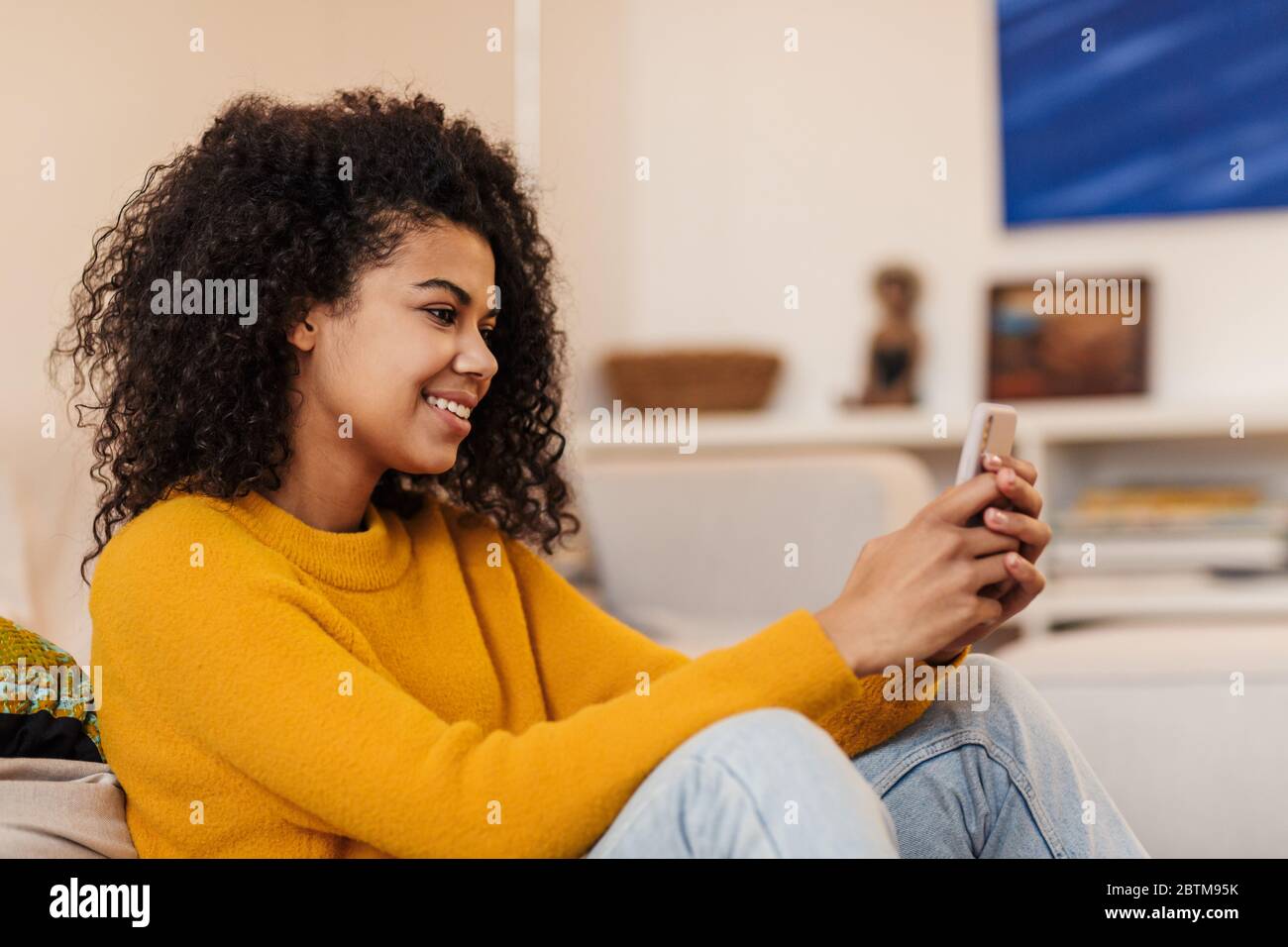 Image of smiling african american woman using cellphone while sitting ...