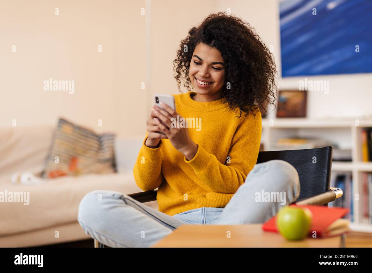 Image of smiling african american woman using cellphone while sitting ...