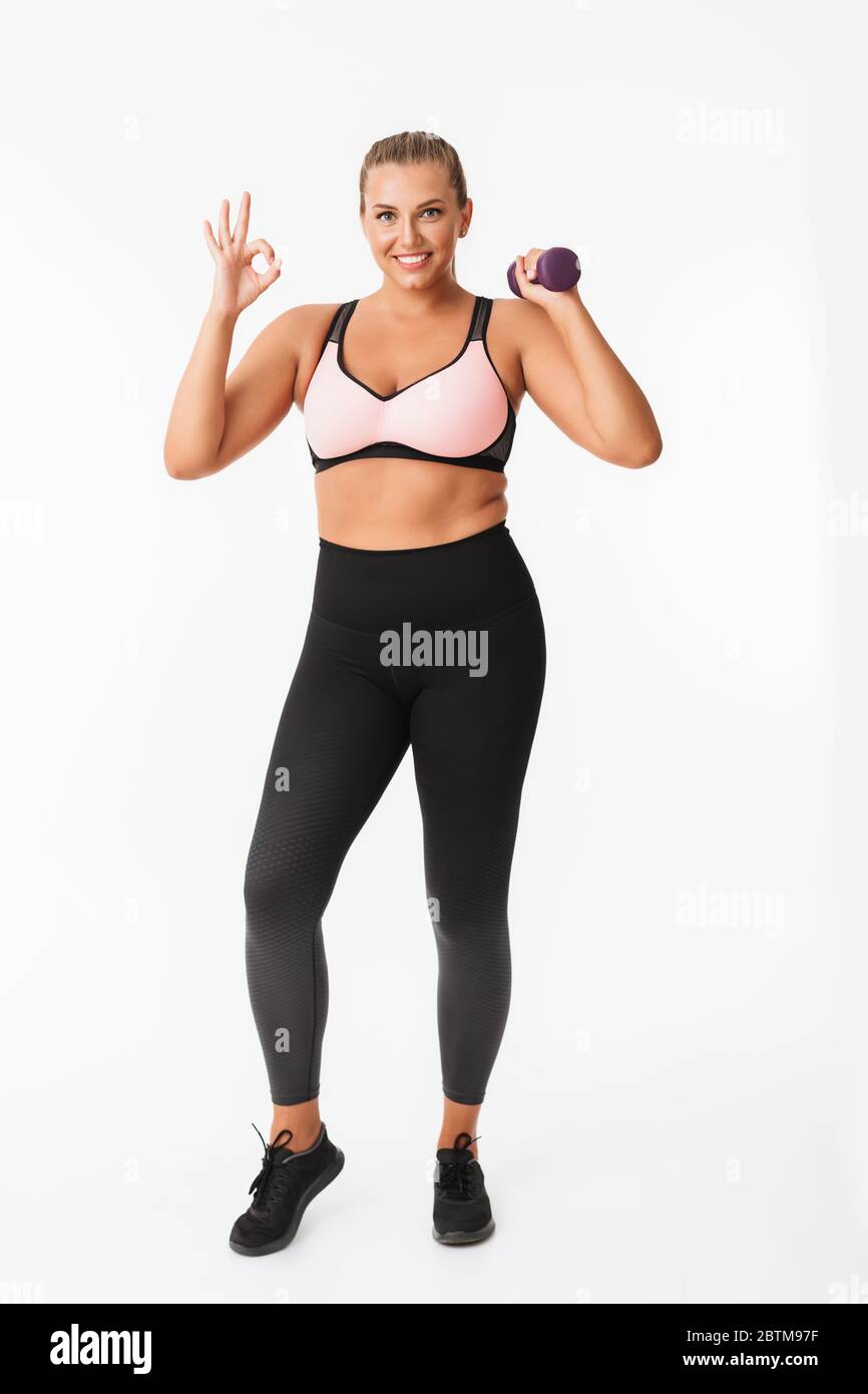 Smiling fat girl in sporty top and leggings holding dumbbells in