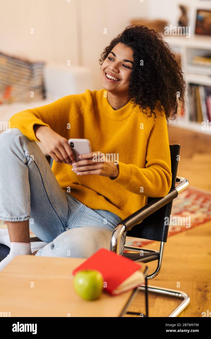 Image of smiling african american woman using cellphone while sitting ...