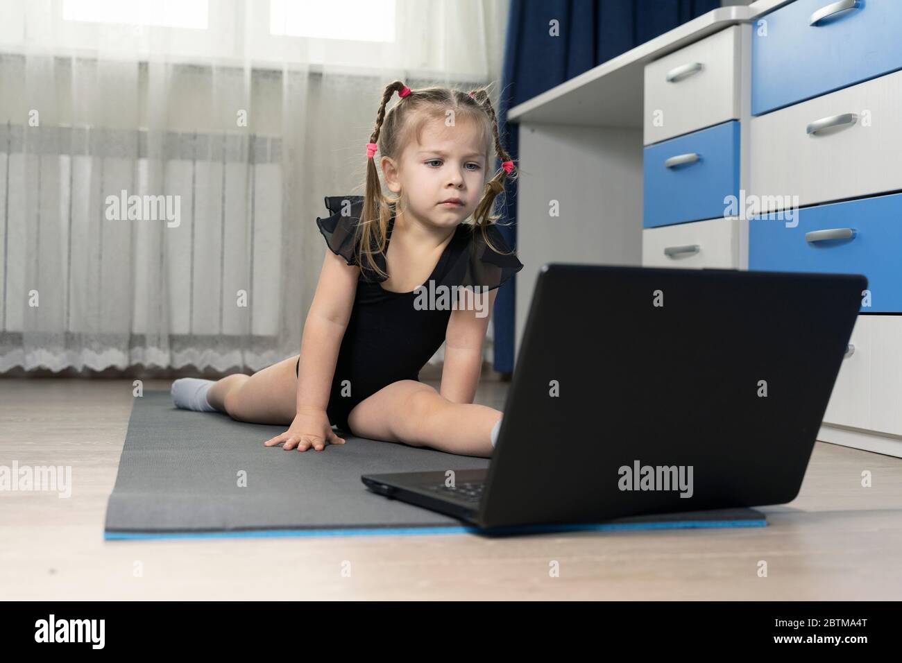 little girl sitting on a twine in front of a laptop at home. online yoga classes on self-isolation at home Stock Photo