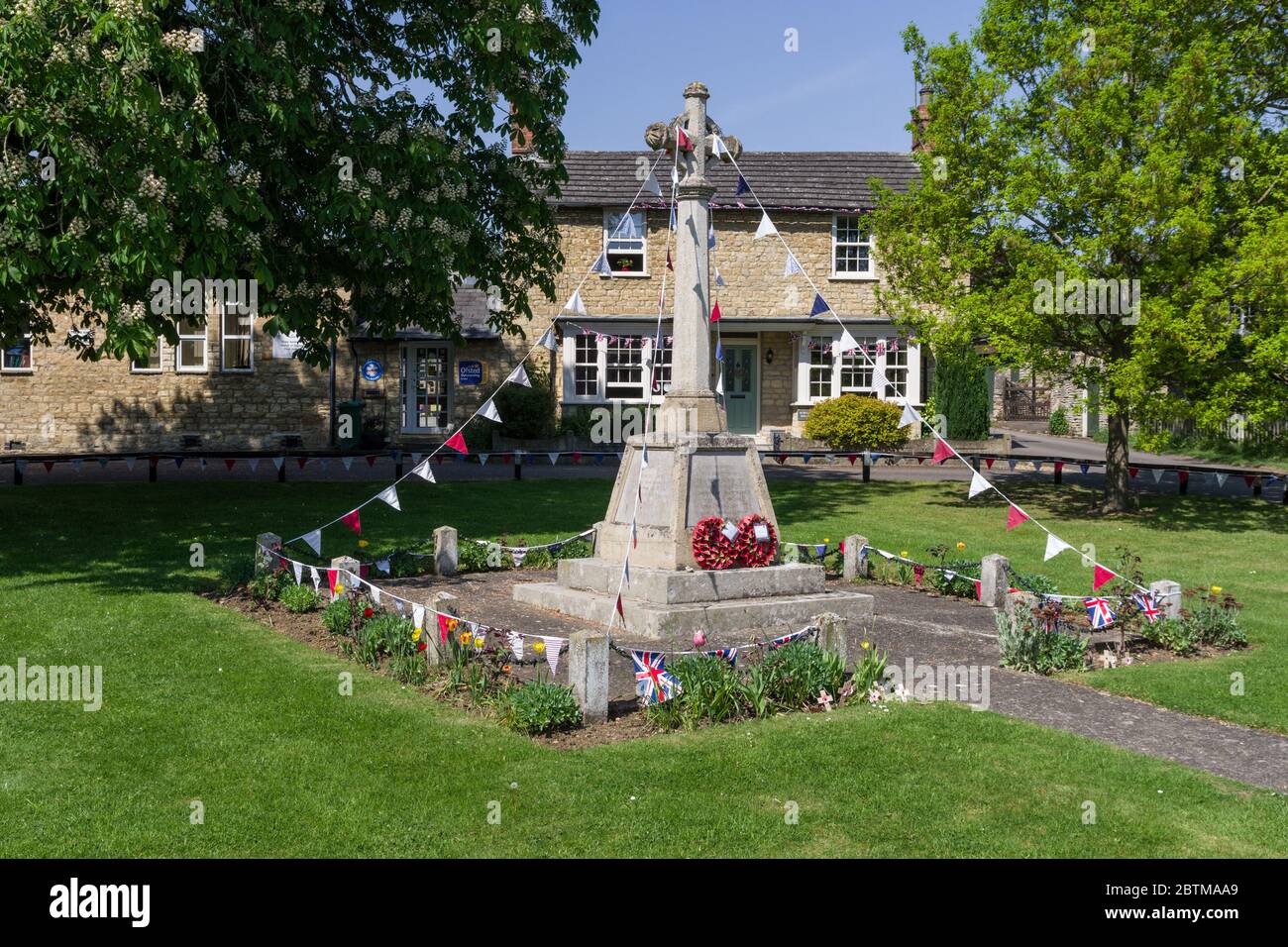 War memorial  covered with bunting to mark VE Day 75th anniversary; the village green, Stoke Goldington, Buckinghamshire, UK Stock Photo