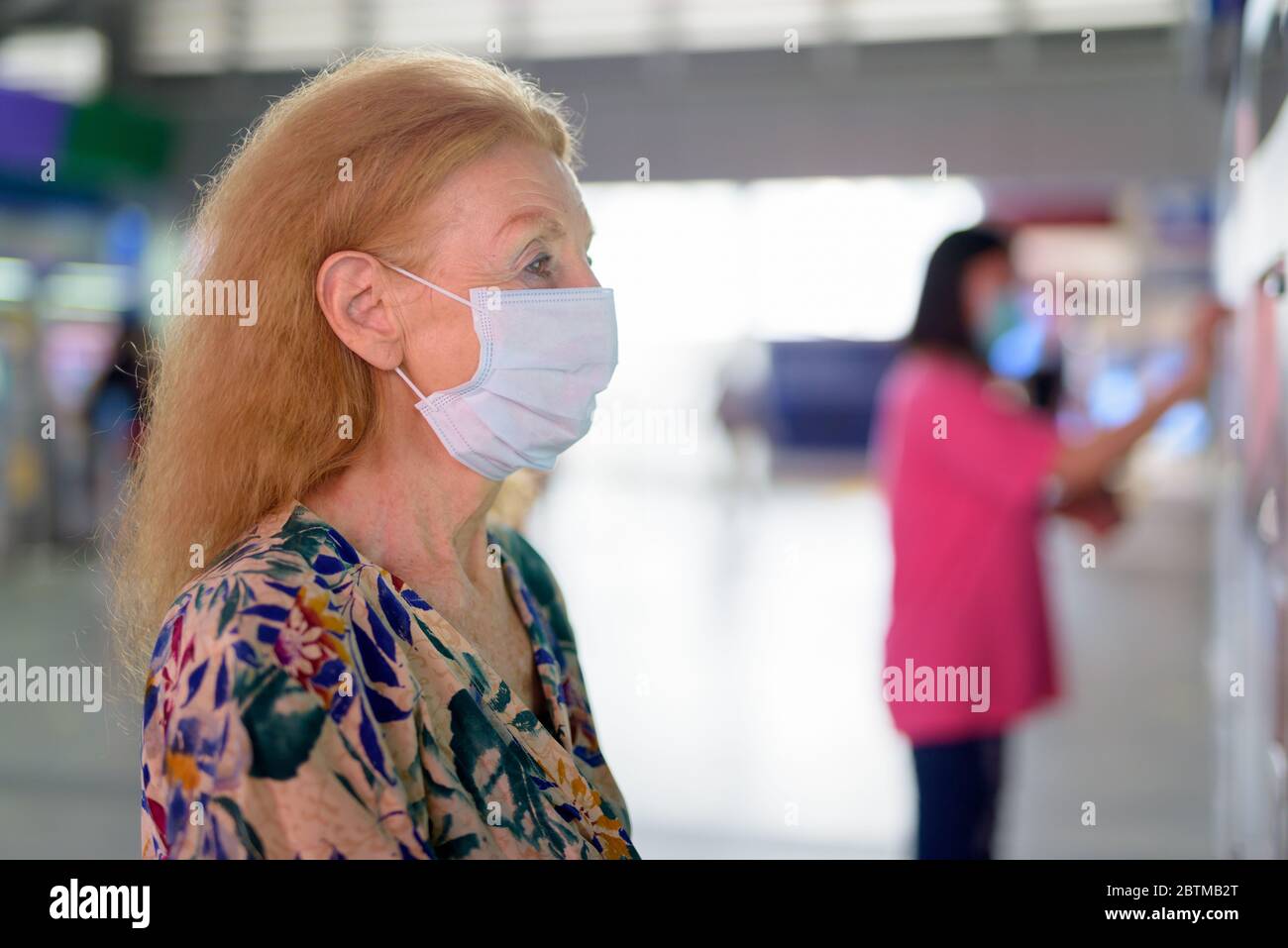 Face of blonde senior woman with mask buying ticket at the sky train ...