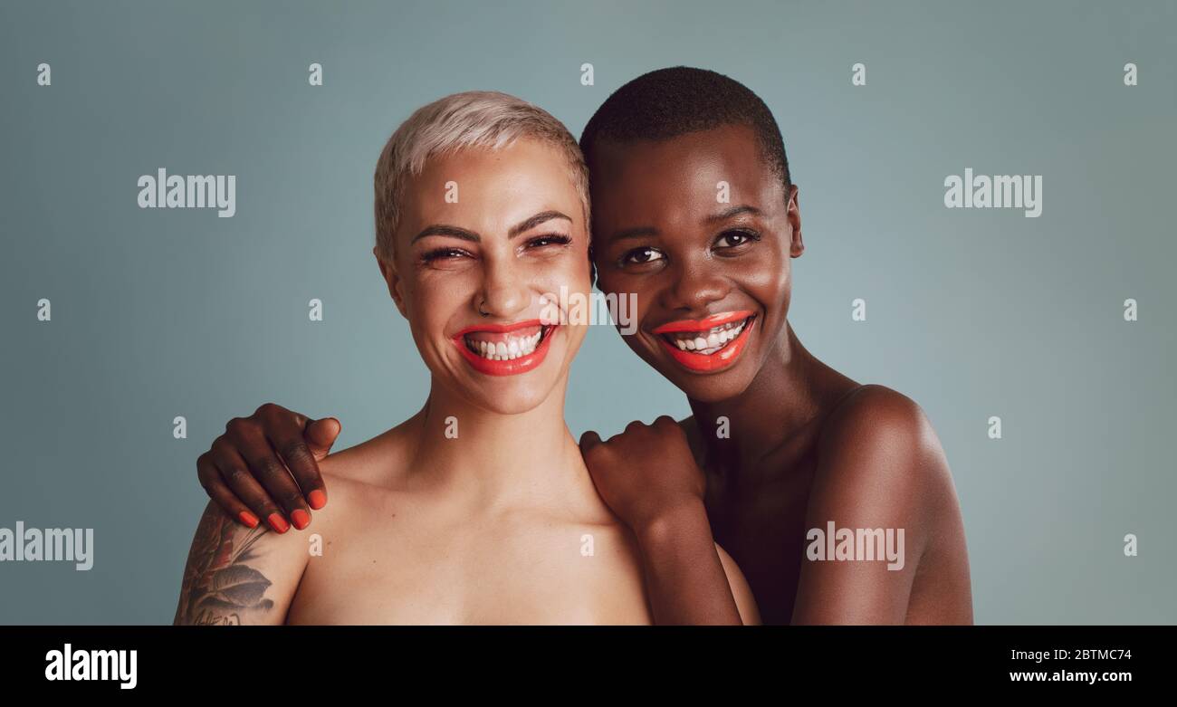 Portrait of two beautiful young women with makeup against a grey background. Female models with short hairstyle looking at camera and smiling together Stock Photo