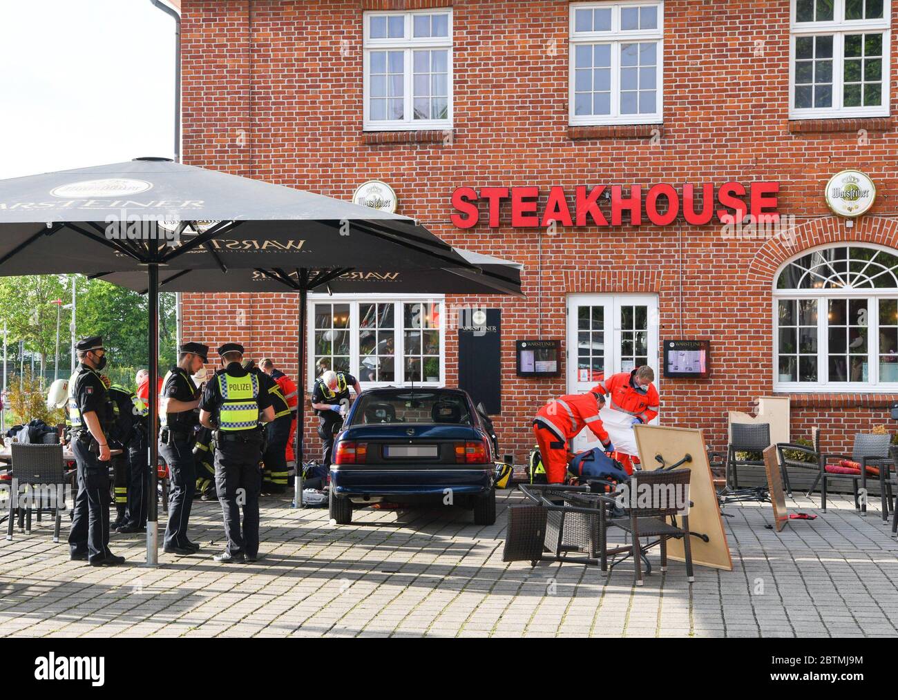 Hamburg, Germany. 26th May, 2020. The accident vehicle is parked between fallen and destroyed furniture in front of a restaurant, while rescue workers care for the injured. A 70-year-old man raced his car onto the terrace of the restaurant, causing fatal injuries to a 48-year-old and serious injuries to a 52-year-old. The two restaurant guests were dragged along by the car and crushed between the car and a wall of the restaurant, according to police reports on 27 May 2020. (to dpa 'Car races in Hamburg on restaurant terrace - three seriously injured') Credit: Joto/dpa/Alamy Live News Stock Photo