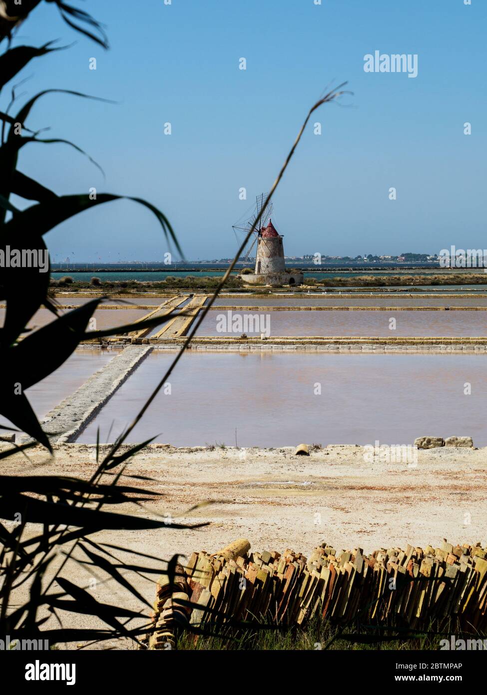 a old windmill and salt pans in sicily with reed in the front Stock Photo