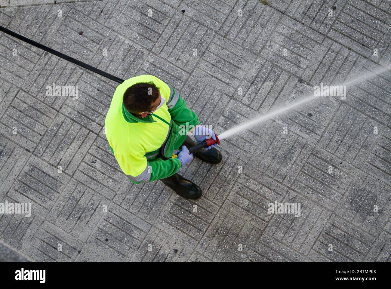 Worker holding a hose cleaning the sidewalk with water. Urban Maintenance or cleaning concept Stock Photo
