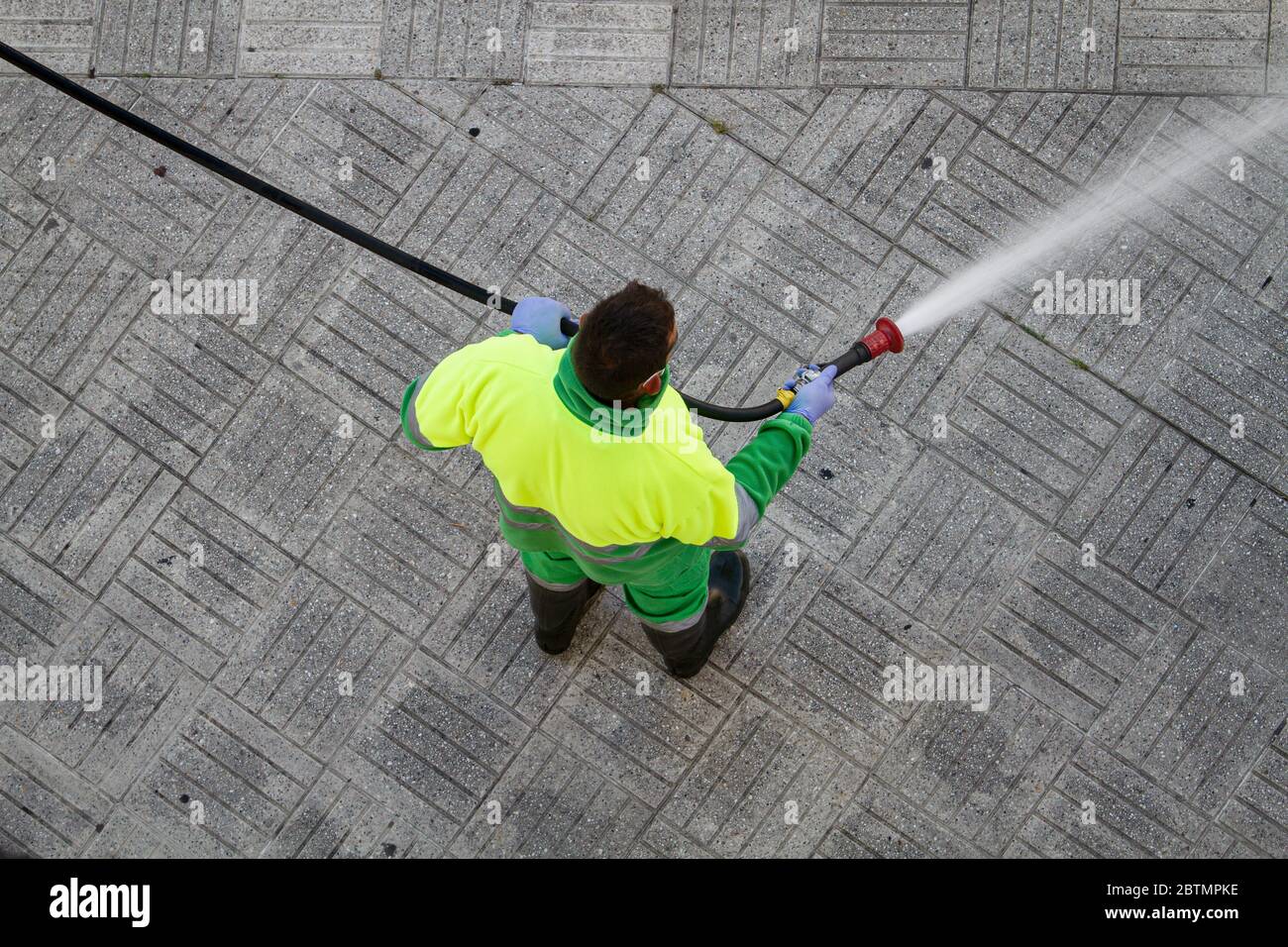 Worker holding a hose cleaning the sidewalk with water. Urban Maintenance or cleaning concept Stock Photo