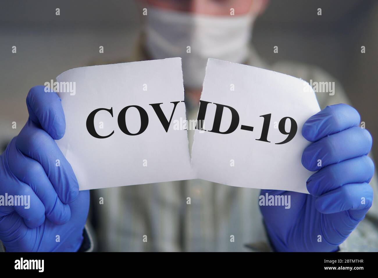 Men's hands in blue gloves tearing paper with the inscription covid-19. Victory over the corona virus. concept of ending the pandemic covid 19 Stock Photo