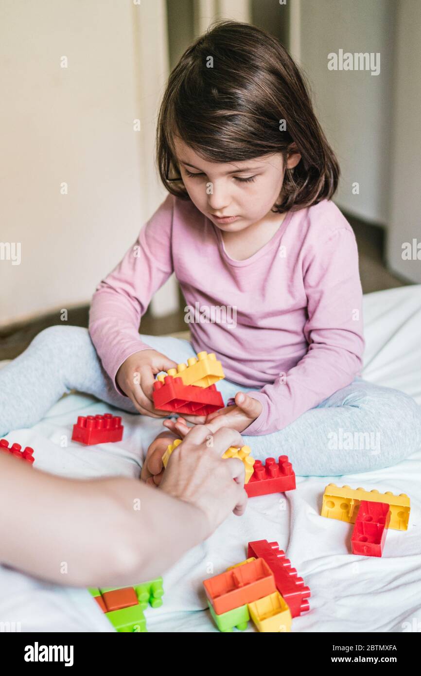 A mother and her daughter sitting down on a bed play games by joining some toy bricks together Stock Photo